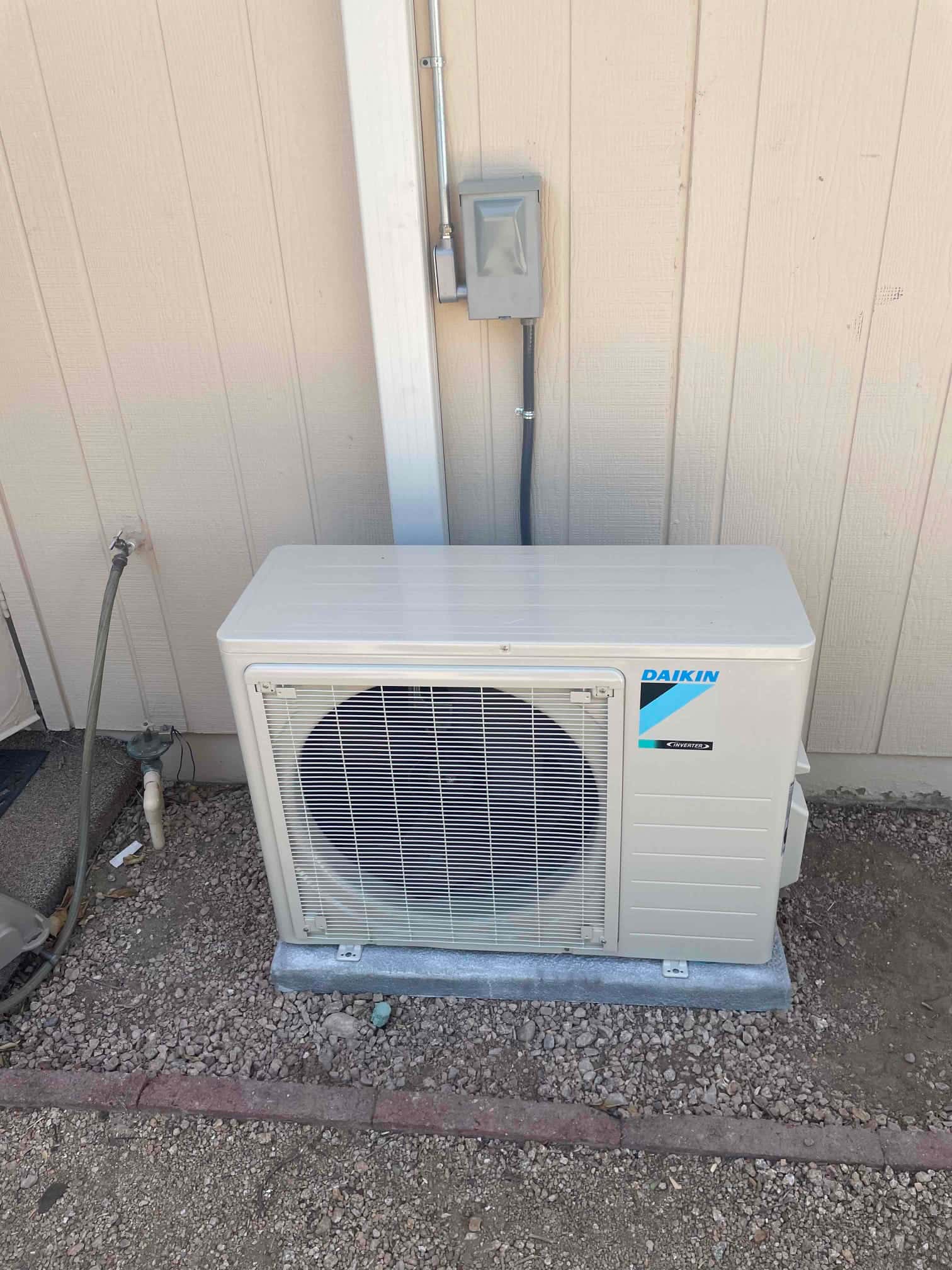 New mini-split outdoor unit set on a level pad with line set cover and weatherproof electrical disconnect mounted beside it.