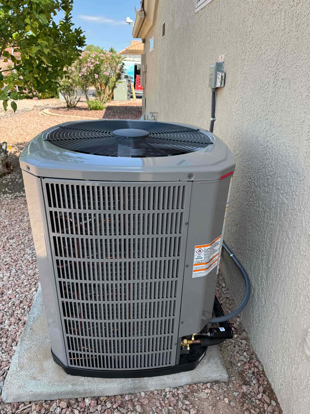 New outdoor condenser set on a level pad with insulated refrigerant line and exterior disconnect mounted on the wall.