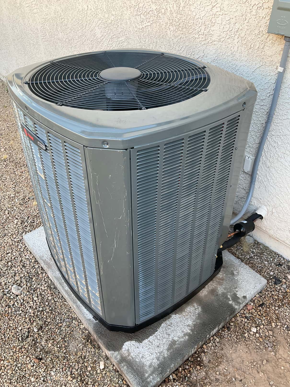 New outdoor condenser set on a level pad with insulated refrigerant lines and electrical whip connected to the wall disconnect.