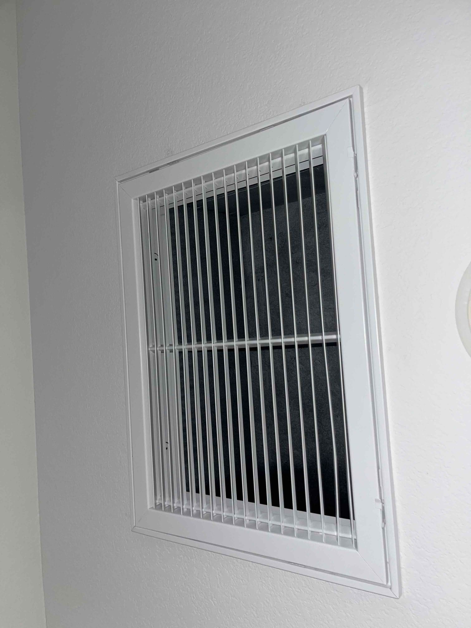New return air grille installed on interior wall, showing clean frame, straight louvers, and dark filter media behind.