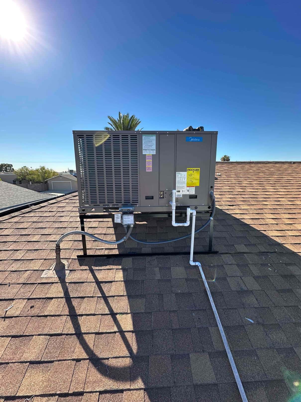 New rooftop package HVAC unit installed on a metal stand with electrical whip, condensate drain, and sealed roof penetrations.