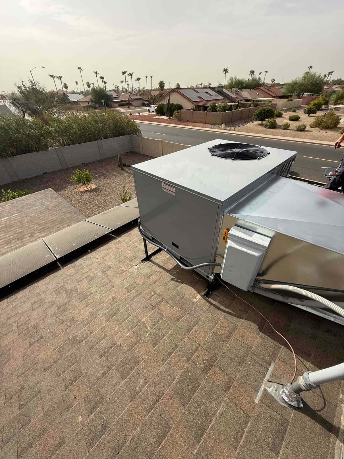 New rooftop package HVAC unit set on a stand with connected duct transition and electrical conduit on a shingle roof.