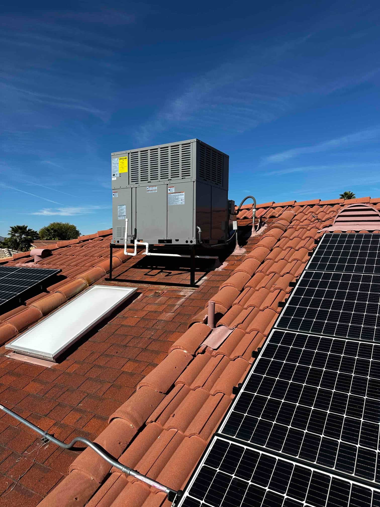 New rooftop package HVAC unit set on a steel stand with connected electrical conduit and drain, alongside existing solar panels.