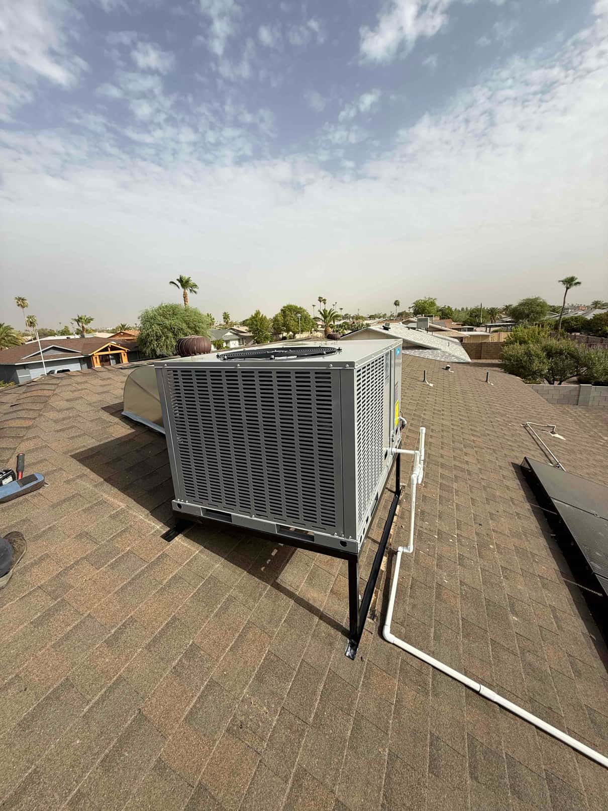 New rooftop package unit mounted on a raised stand with insulated refrigerant lines and condensate drain routed along the roof.