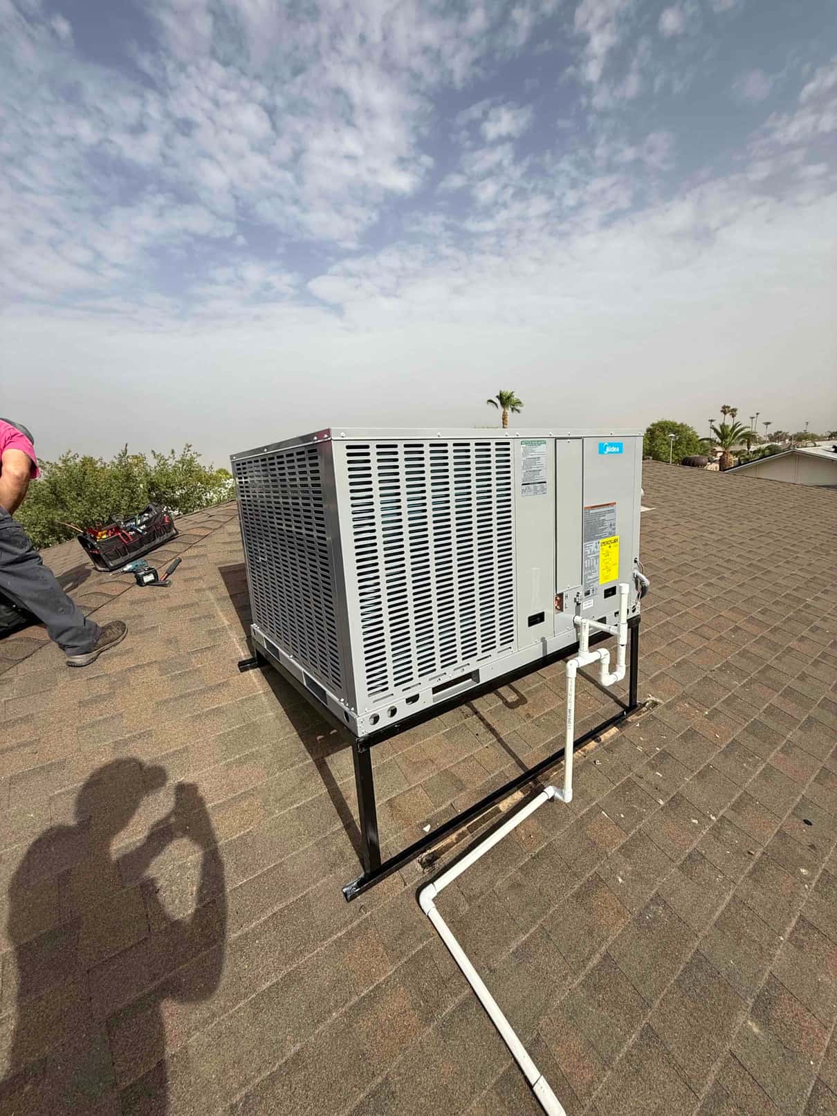 New rooftop package unit set on a steel stand with connected PVC condensate drain routed across the shingles.