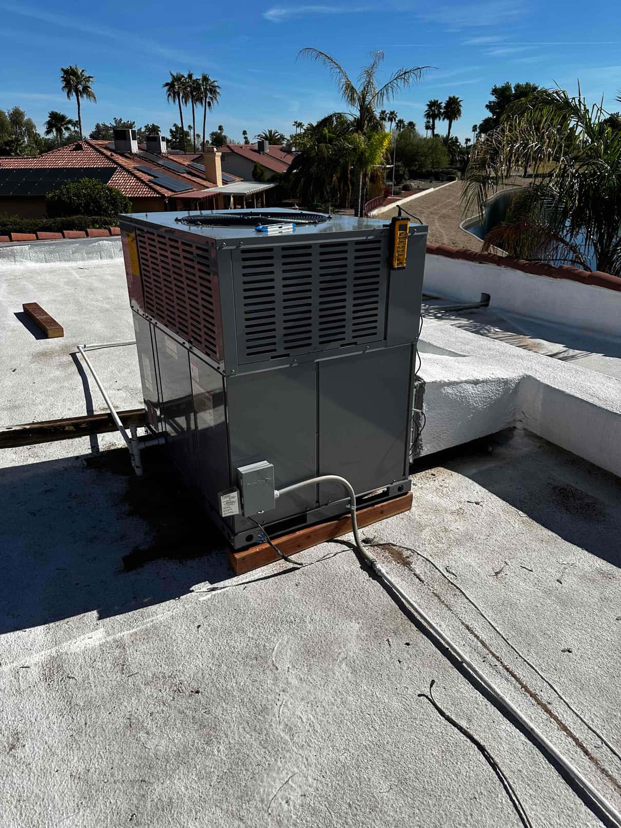 New rooftop packaged HVAC unit installed on wood risers with electrical disconnect and condensate drain connected.