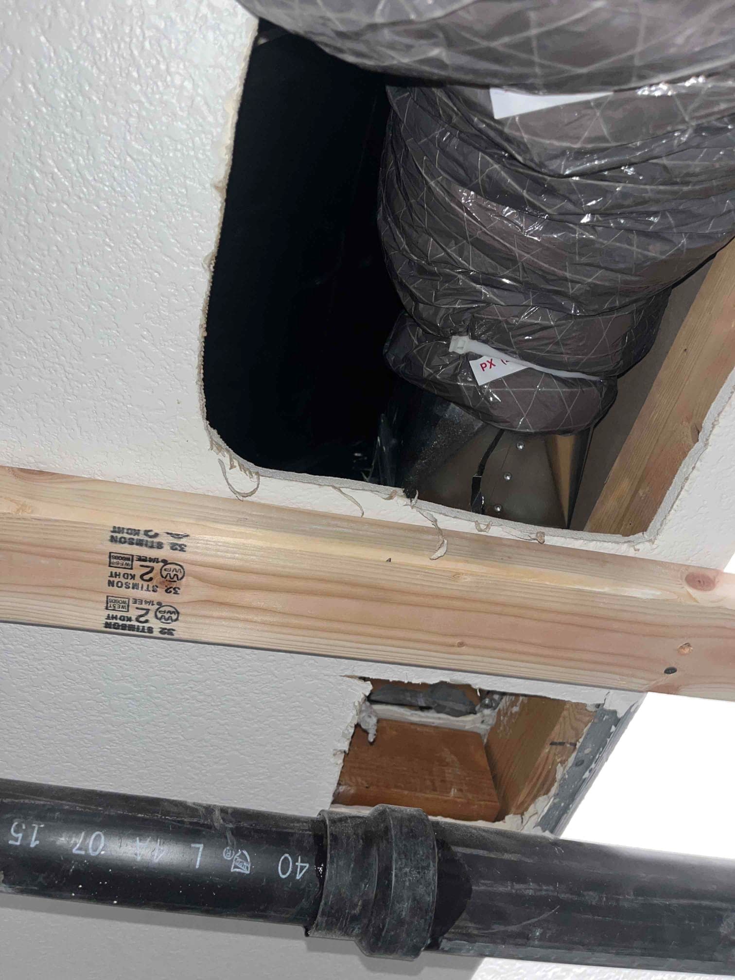 Open ceiling cutout exposes insulated flexible supply duct and framing during duct relocation, with adjacent plumbing pipe visible below.
