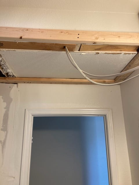 Open ceiling framing above a doorway shows relocated supply duct area with new wiring routed along the joists.