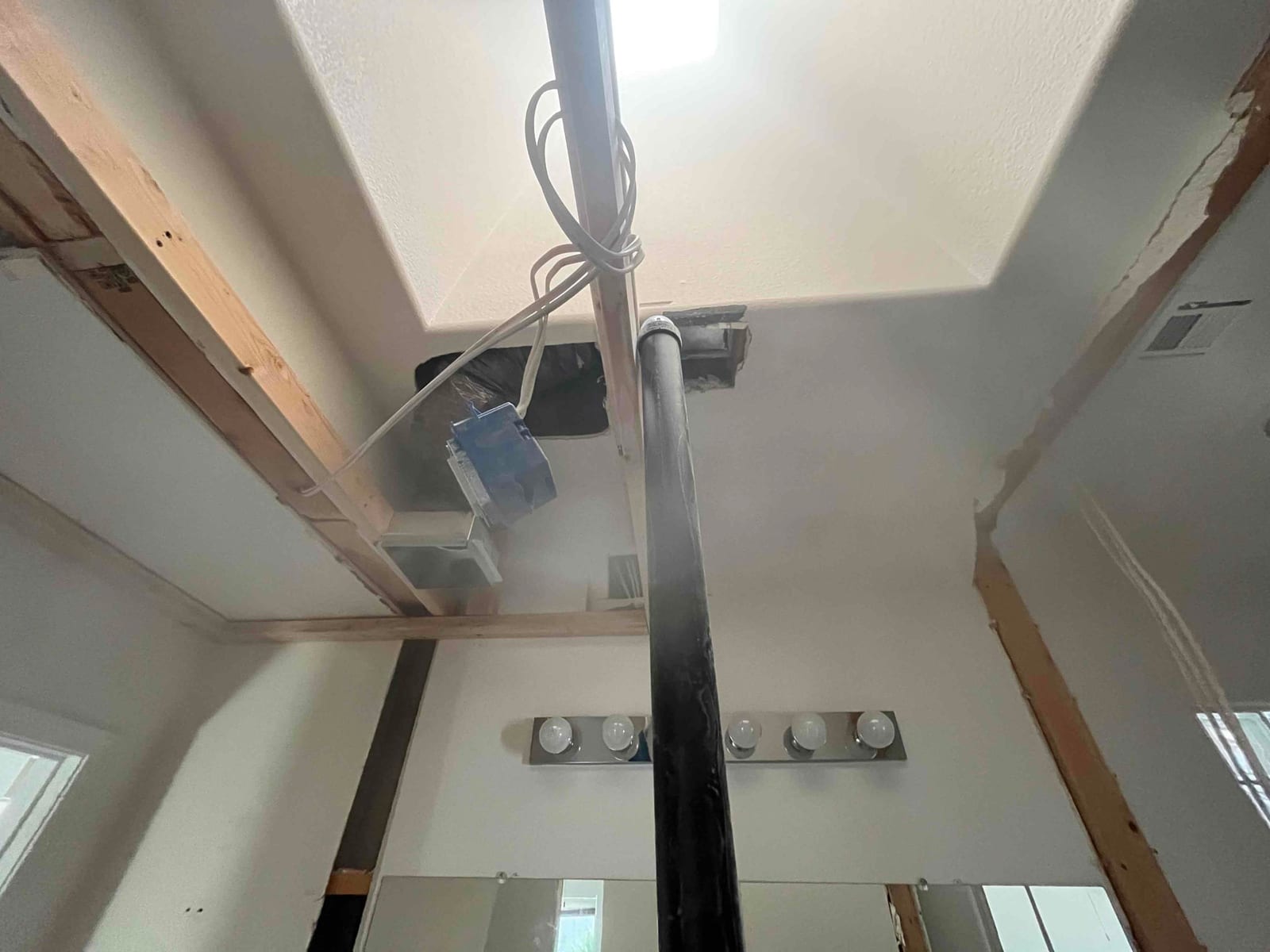 Open ceiling shows relocated flexible supply duct and new return filter frame area with exposed framing above a bathroom vanity.
