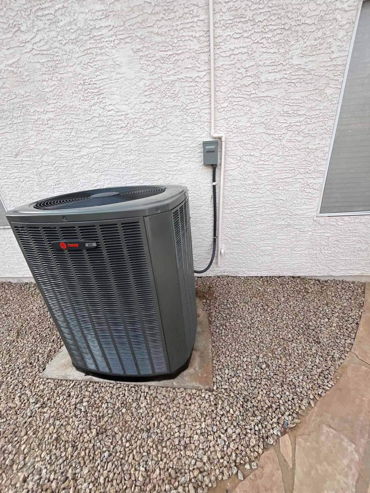 Outdoor condenser set on a level pad with armored electrical whip and weatherproof disconnect mounted on the exterior wall.