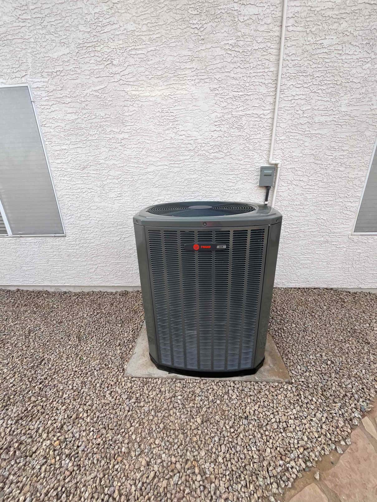 Outdoor condenser set on a level pad with electrical whip and disconnect mounted on the stucco wall.