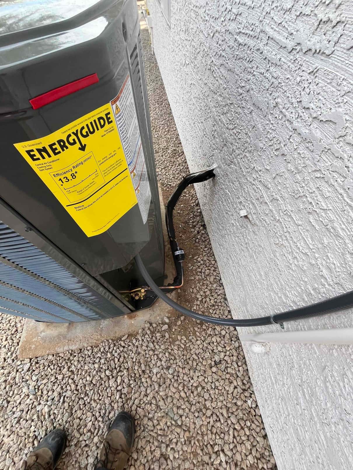 Outdoor condenser set on a level pad with insulated refrigerant lines and sealed wall penetration beside the unit.