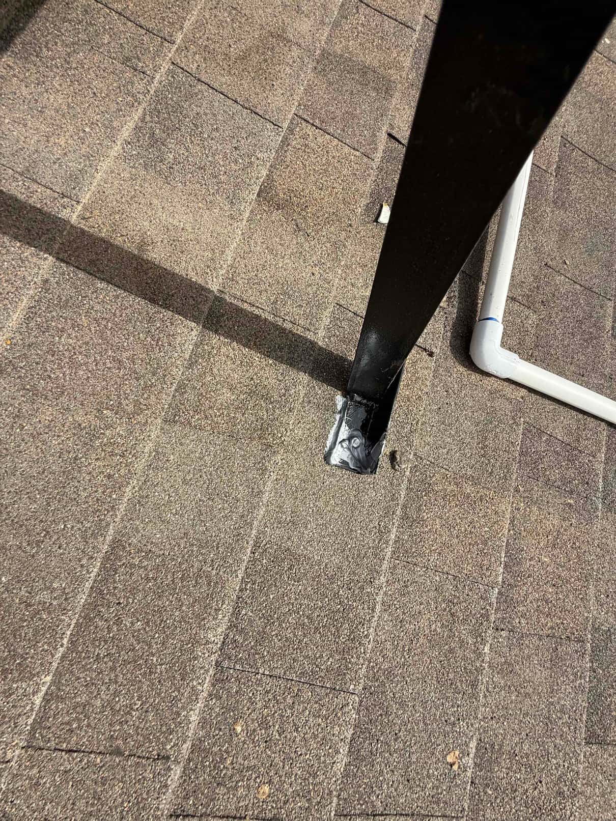 Rooftop mounting post penetrates shingles with sealant applied, next to PVC condensate drain line elbow during install.