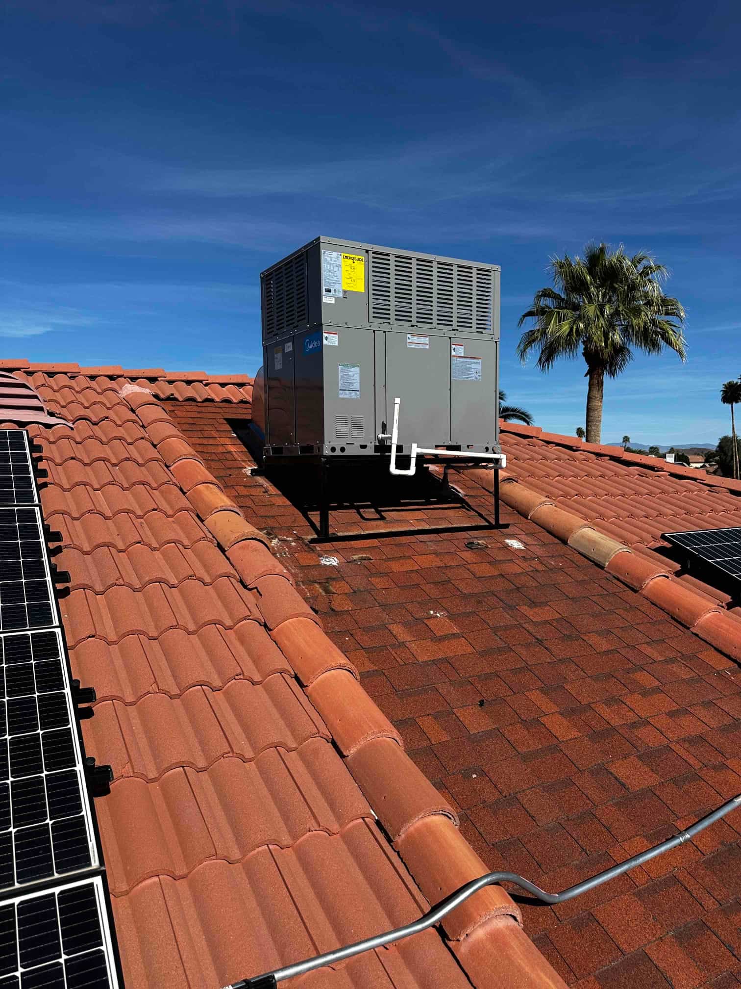 Rooftop packaged HVAC unit installed on a raised stand with insulated condensate drain and adjacent solar panels visible.