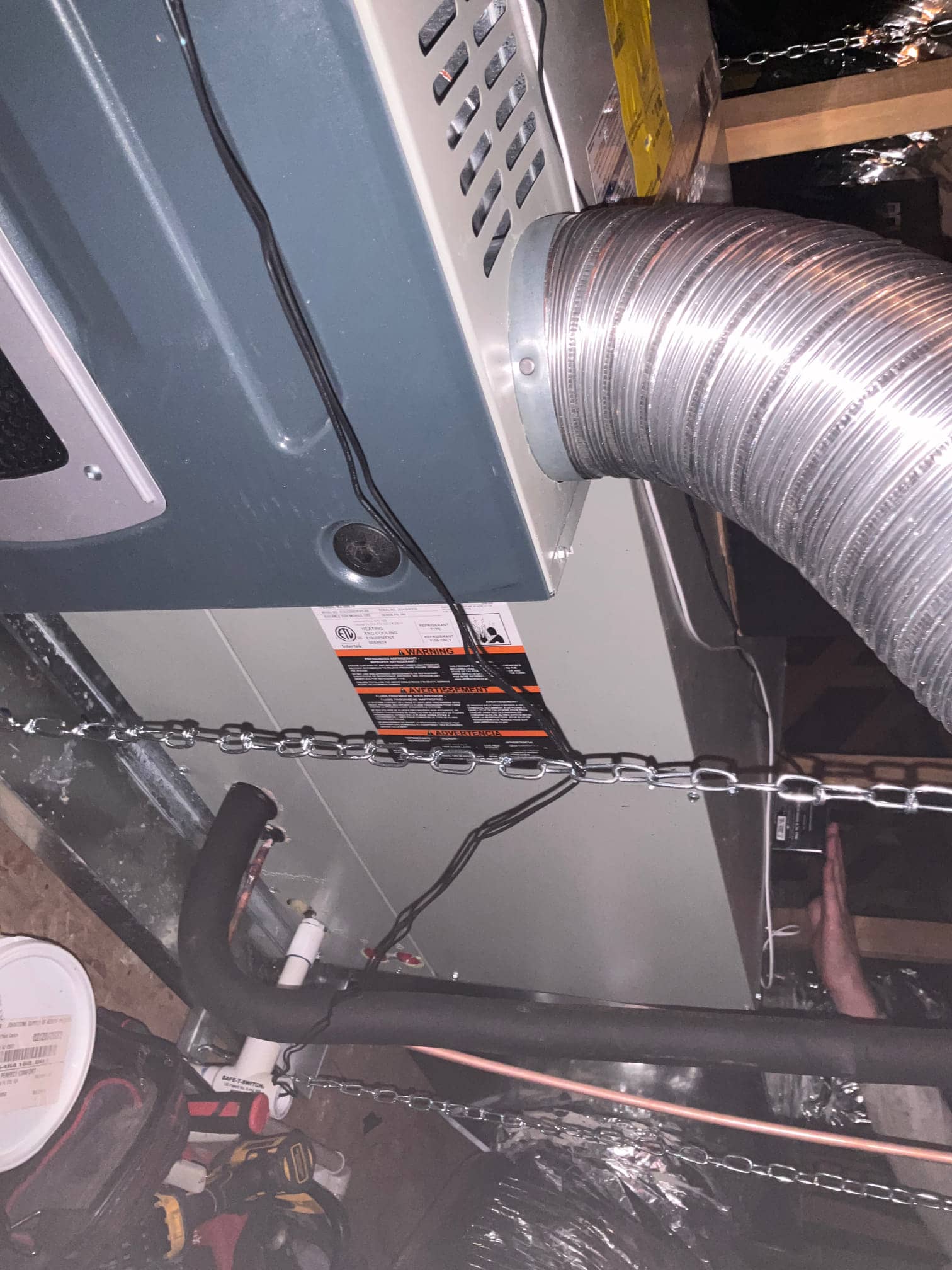 Suspended air handler installed with insulated refrigerant lines, condensate drain, flexible duct connection, and hanging chains in the attic.