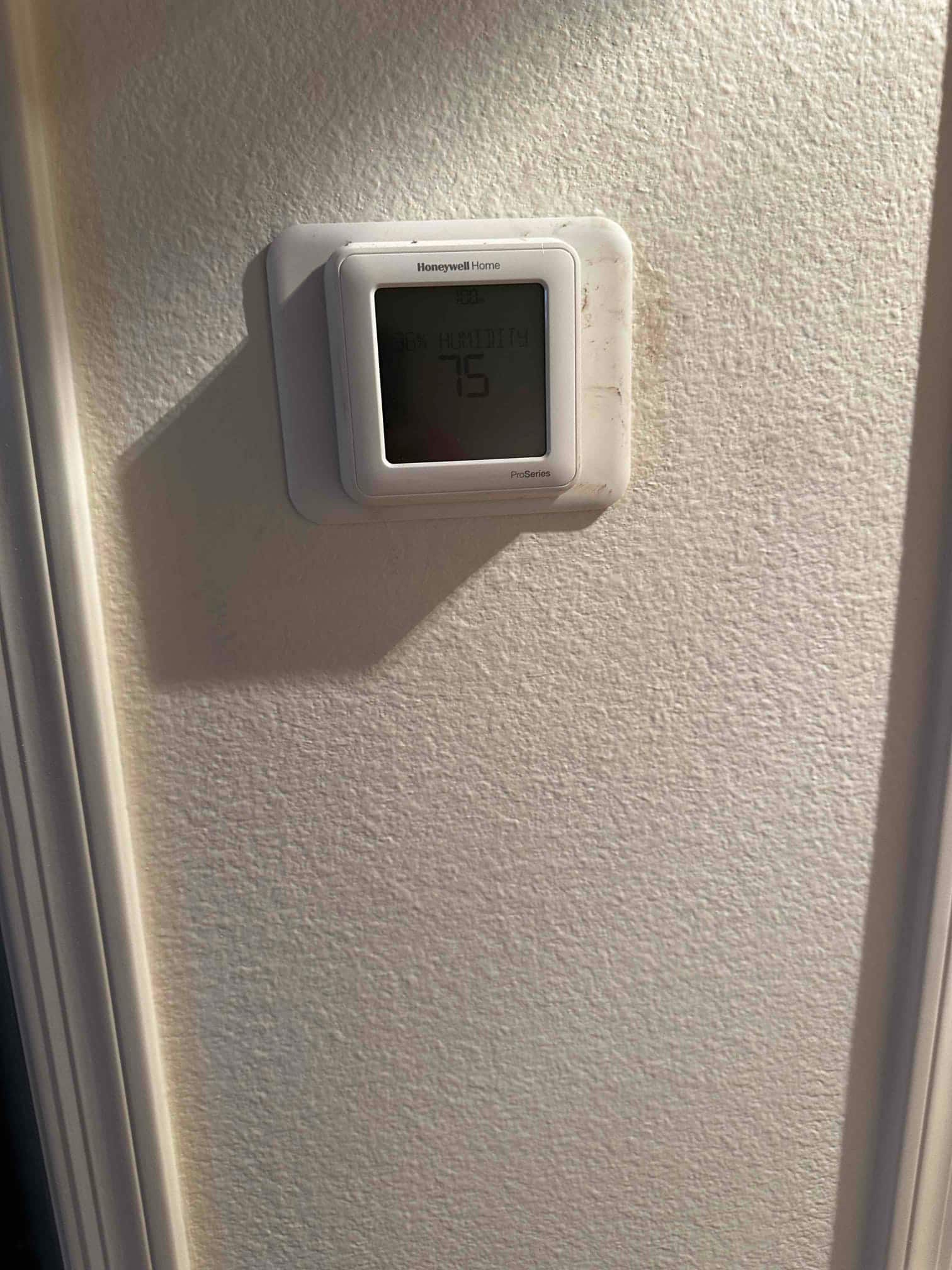 Wall-mounted digital thermostat installed and powered, displaying room temperature and humidity on its screen.