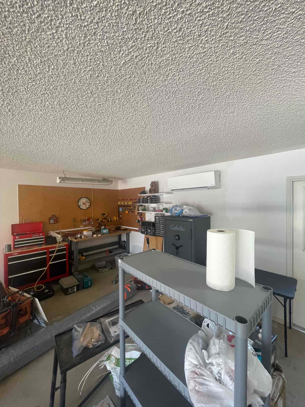 Wall-mounted mini-split indoor unit installed in a garage workshop above benches and storage, with line set penetration sealed.