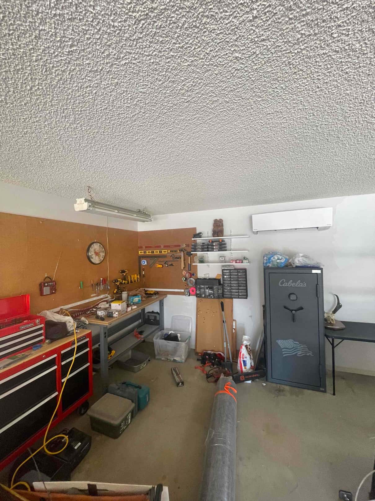 Wall-mounted mini-split indoor unit installed in a garage workshop above benches and tools, showing the completed head placement and routing area.