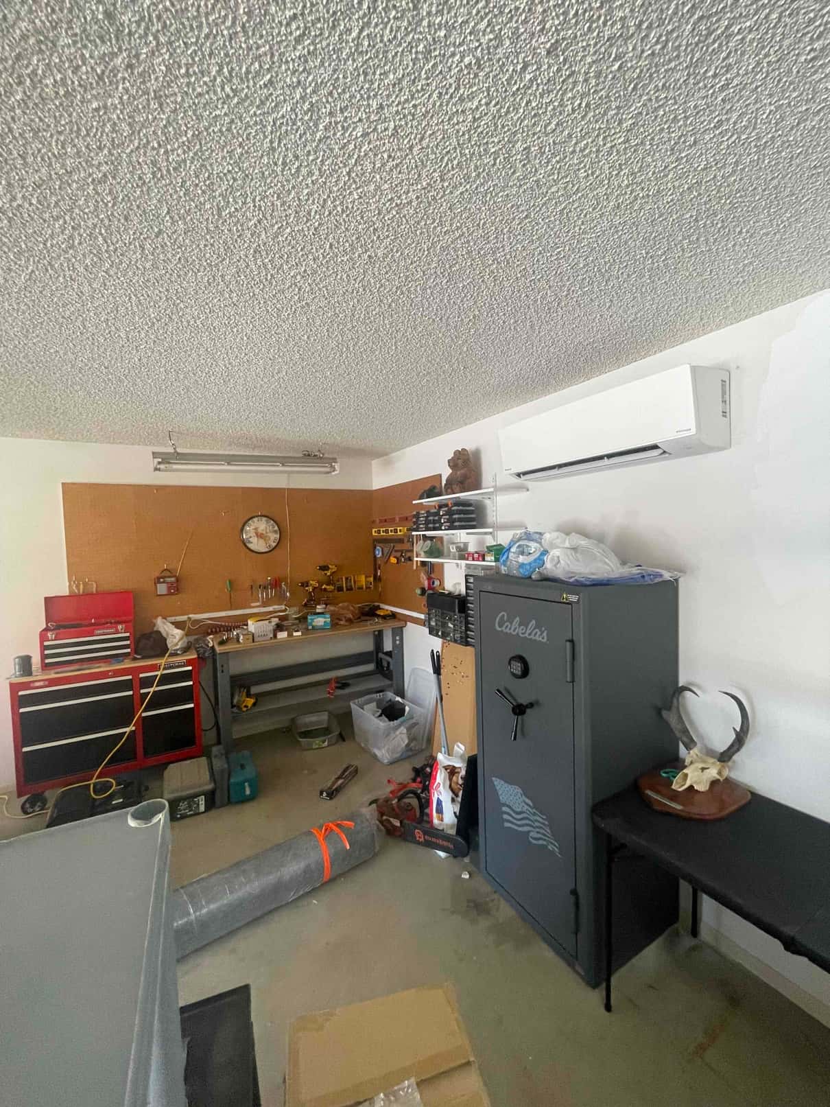 Wall-mounted mini-split indoor unit installed in a garage workspace, with tools and equipment visible around the completed area.