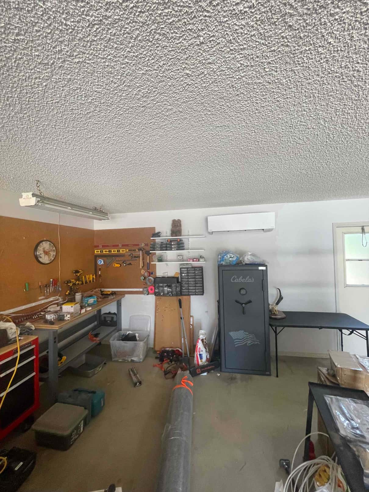 Wall-mounted mini-split indoor unit installed above a workbench in a garage, with tools and equipment organized below.