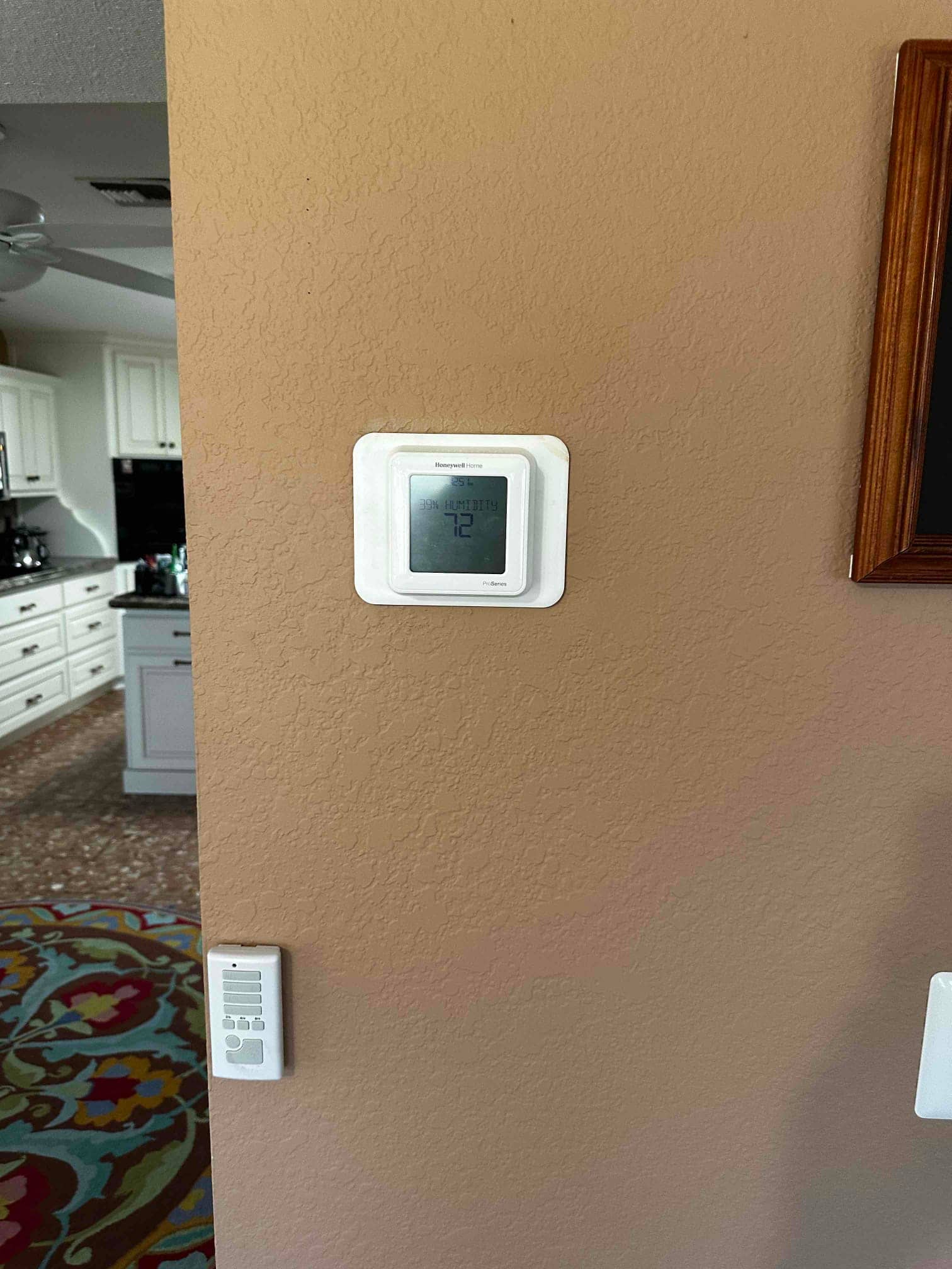 Wall-mounted thermostat installed and powered on, with adjacent control device below, shown in a finished interior space.