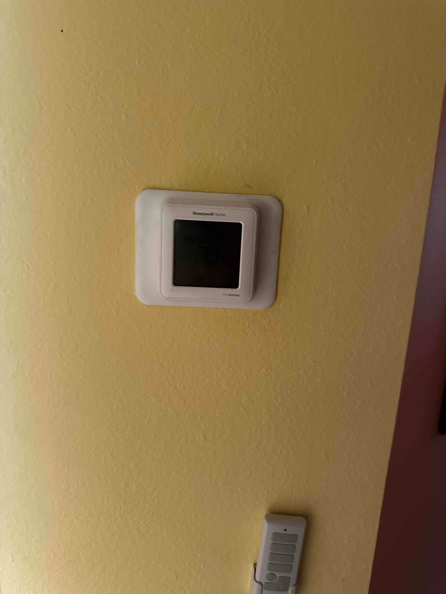 Wall-mounted thermostat installed and powered on, showing the display against a finished interior wall.
