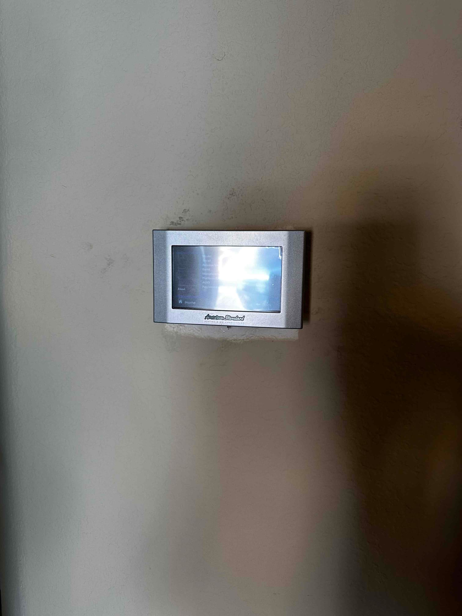 Wall-mounted touchscreen thermostat installed and powered on, showing the new control interface for the HVAC system.
