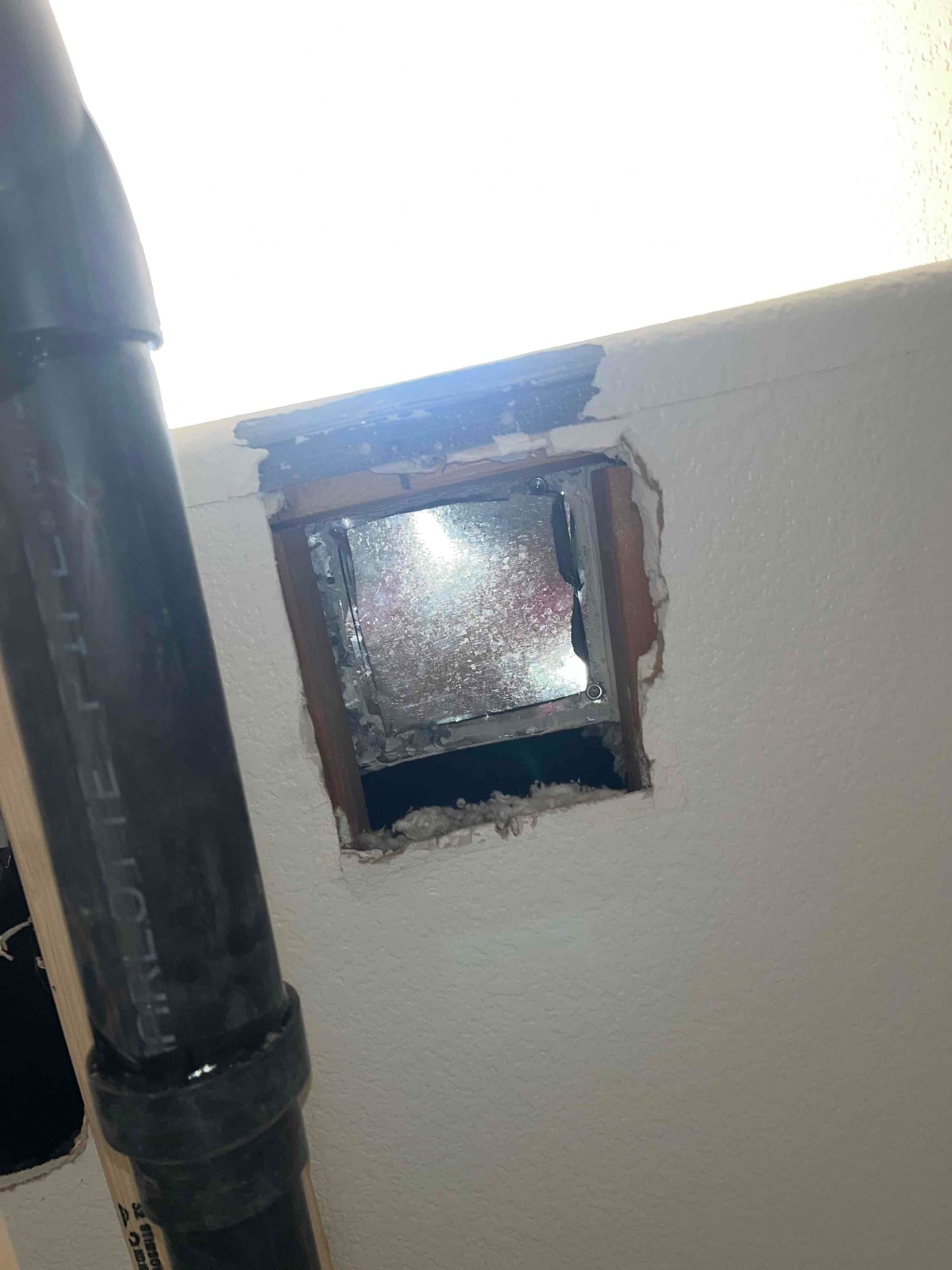 Wall opening exposes metal duct interior with rough drywall edges during supply duct relocation work.