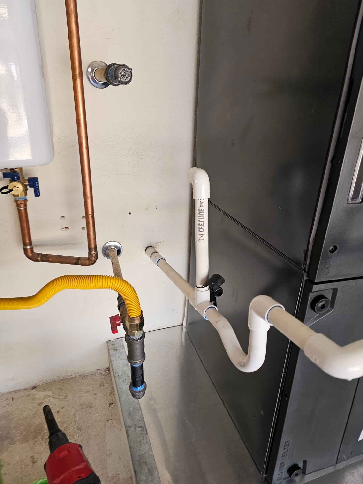 Air handler installed with PVC condensate drain, cleanout, and nearby gas and water lines neatly routed and secured.