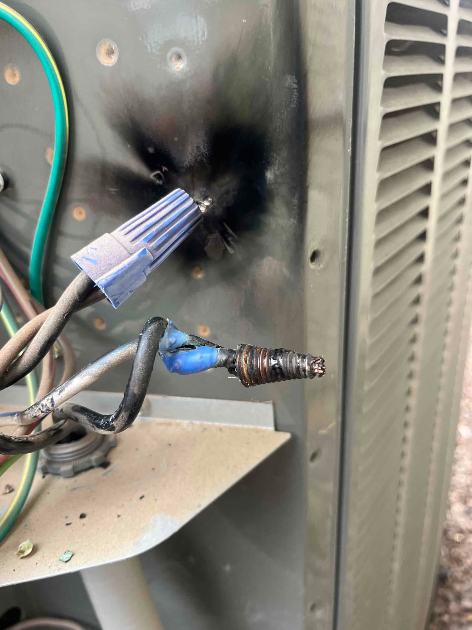 Burnt wire connection at the outdoor condenser panel showing a damaged wire nut and scorched metal surface.