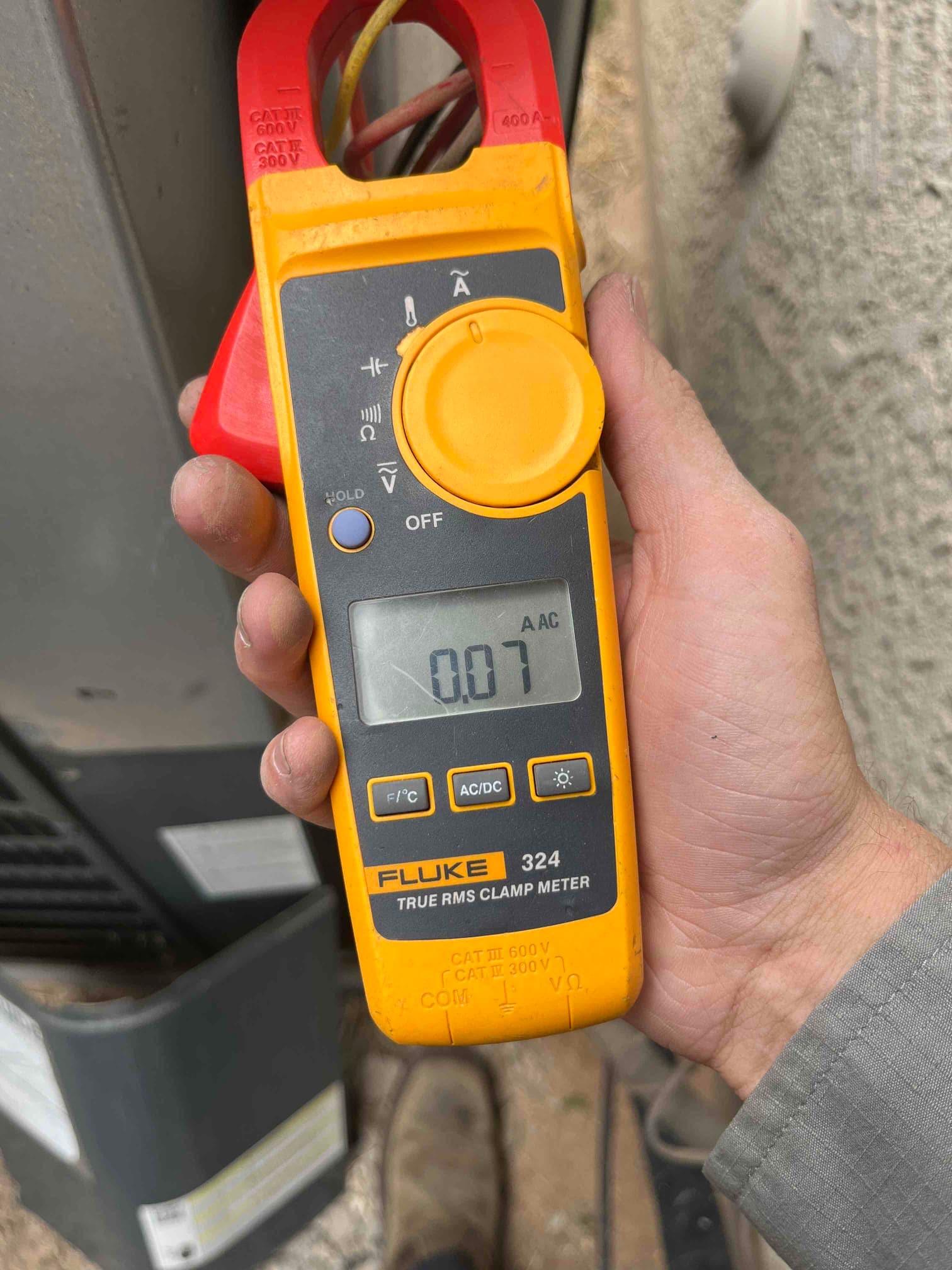Clamp meter measures AC current on a conductor, displaying 0.07 A on the screen.