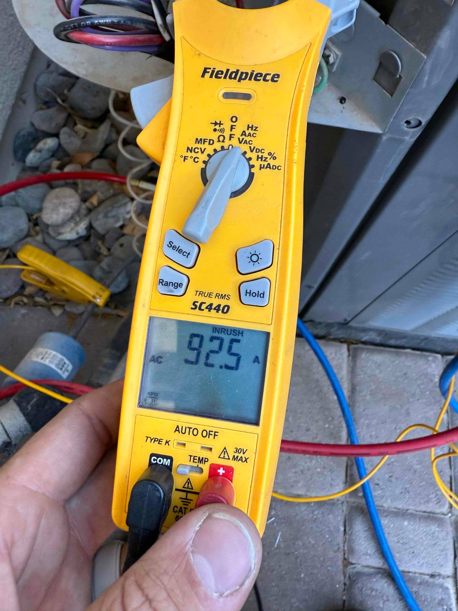 Clamp meter set to INRUSH shows 92.5 A while measuring current on the air conditioner’s electrical conductors.