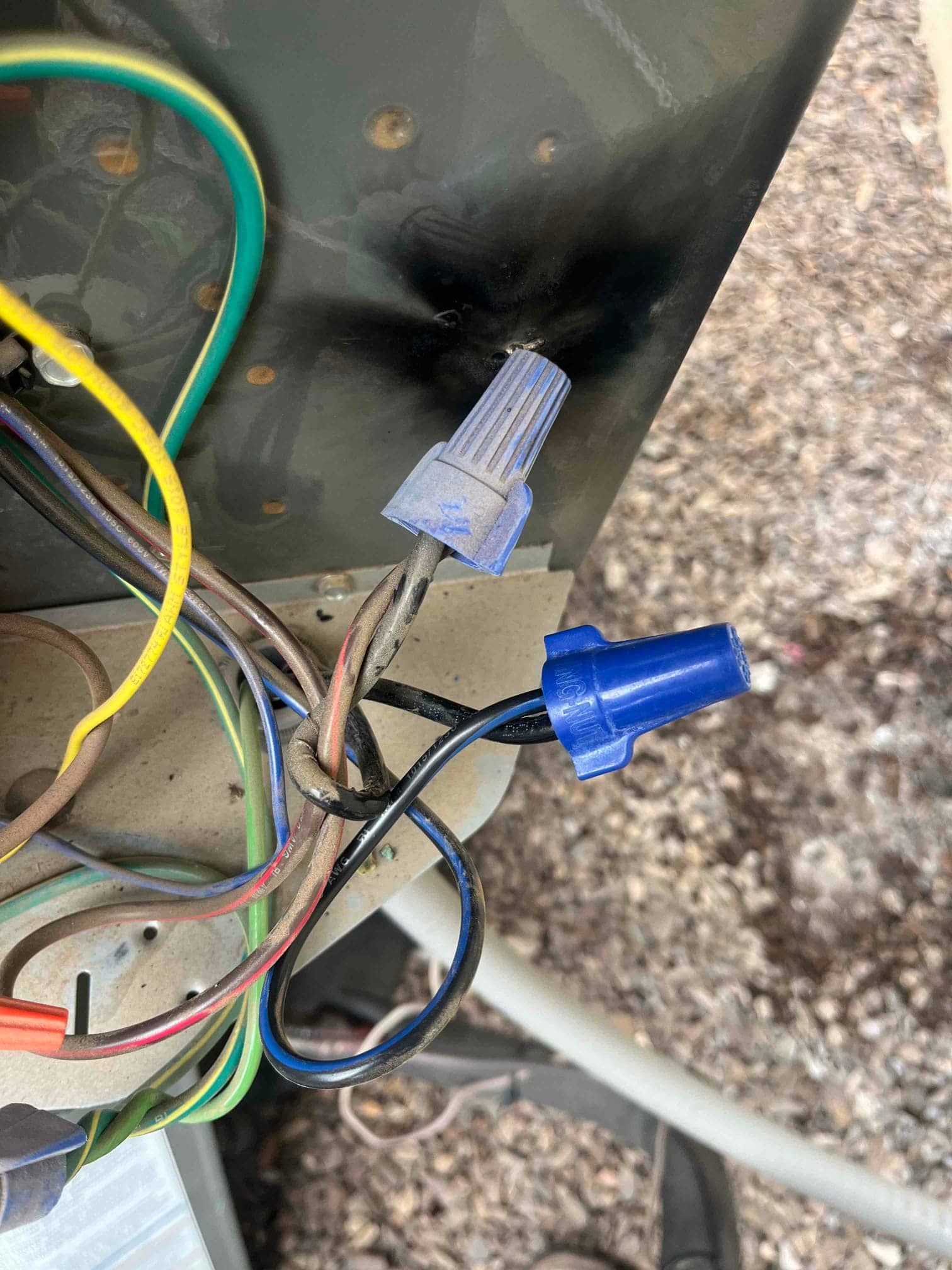 Close-up of electrical wiring with blue wire nuts securing splices inside the outdoor condenser cabinet.