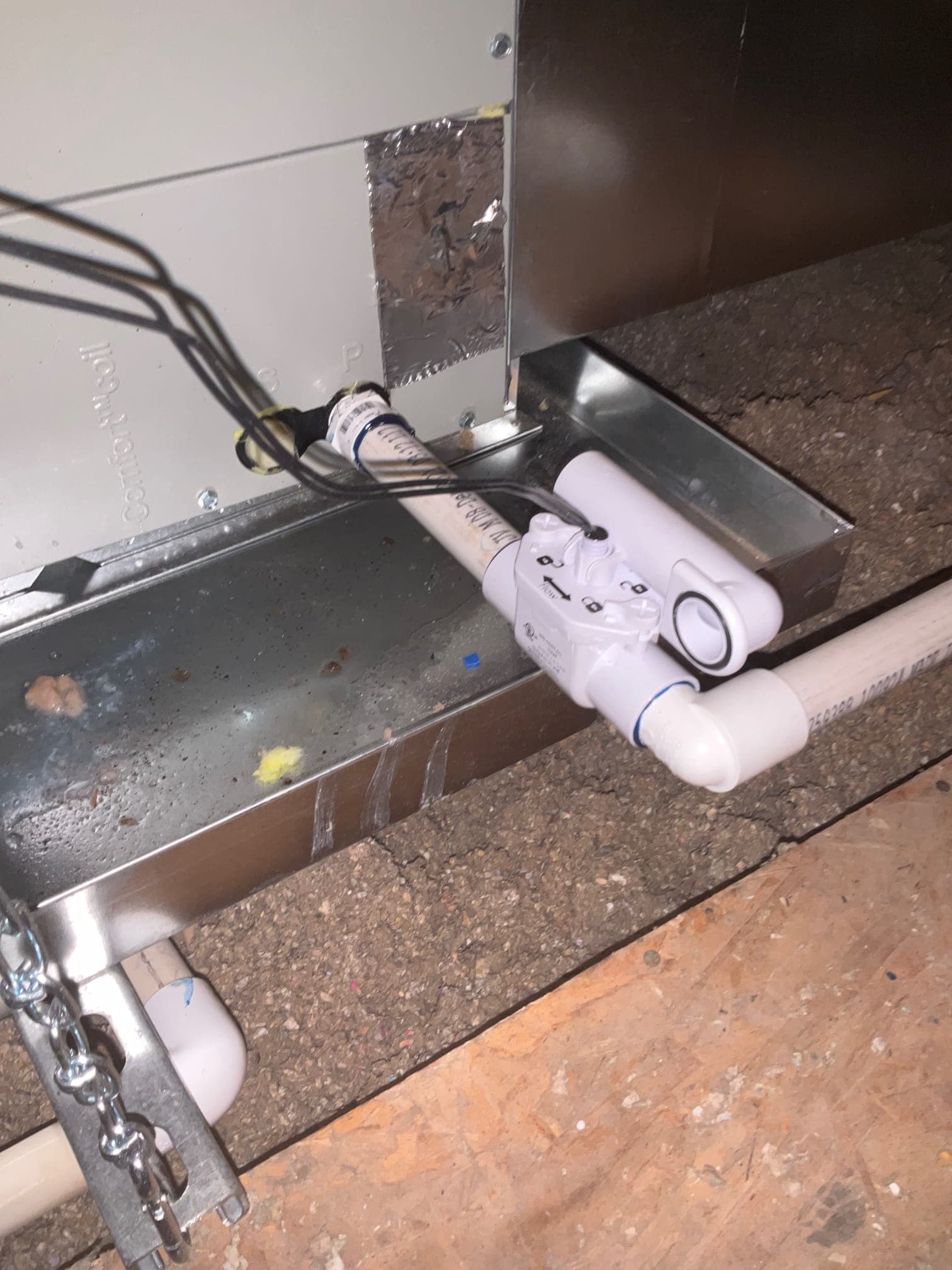 Condensate drain assembly with float safety switch connected to the air handler over a metal secondary drain pan.
