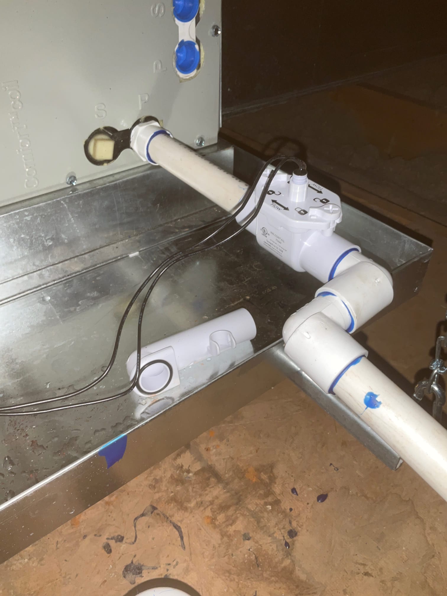 Condensate drain assembly with float safety switch installed on the auxiliary pan beneath the air handler, with PVC piping and fittings.