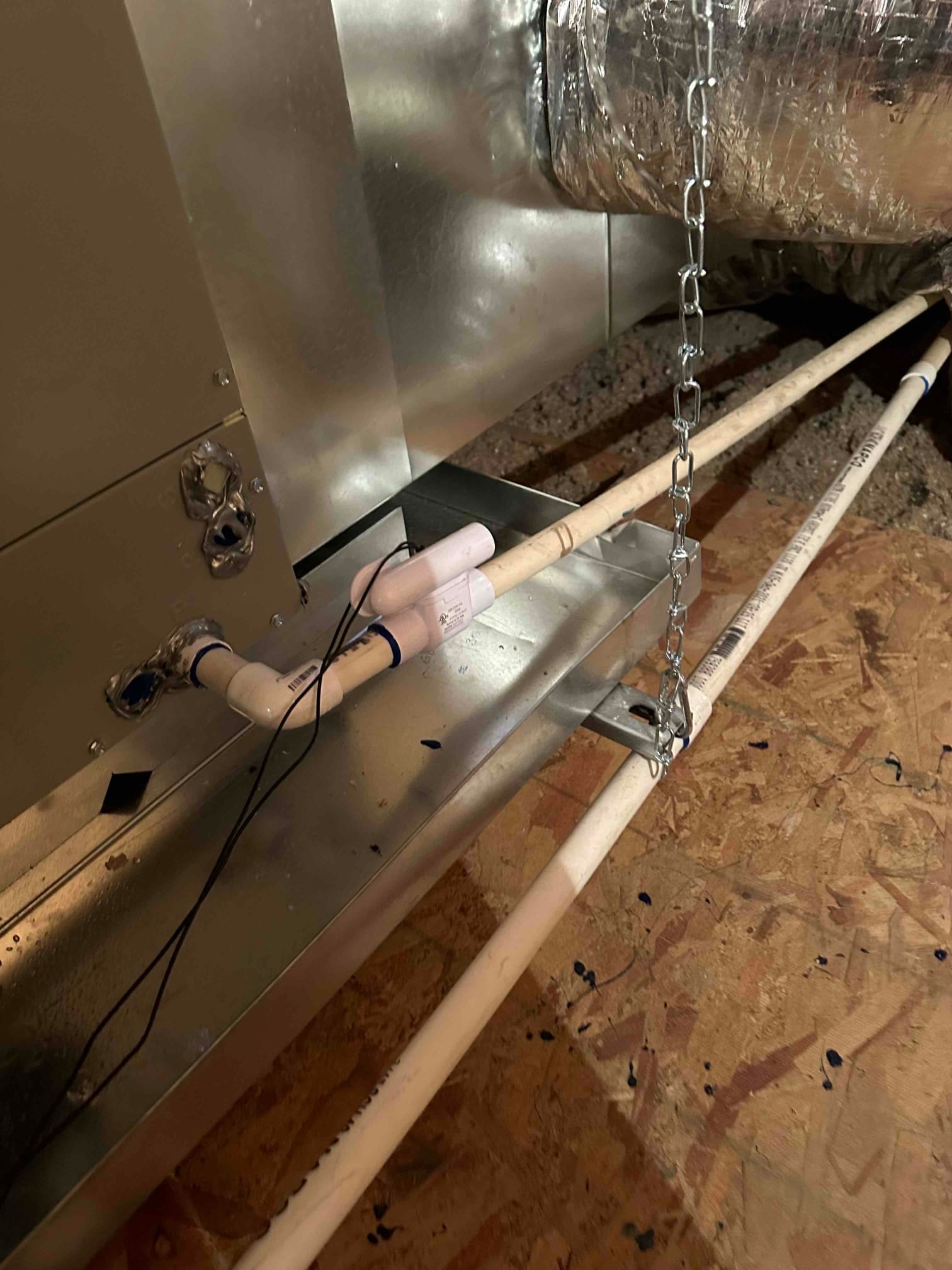 Condensate drain piping connected to the indoor unit with a cleanout and secondary drain over a metal drain pan in the attic.