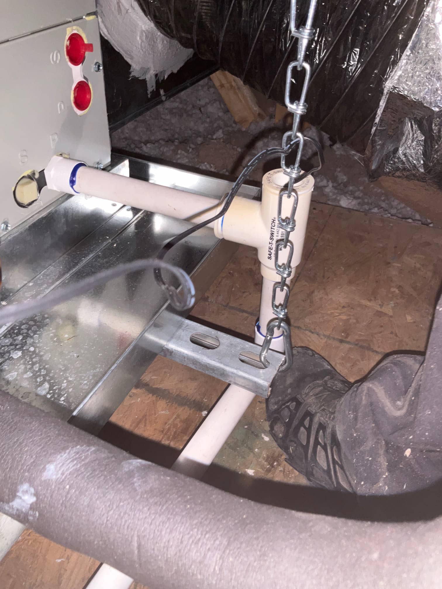 Condensate drain piping with a float safety switch connected to an air handler on a suspended platform in the attic.