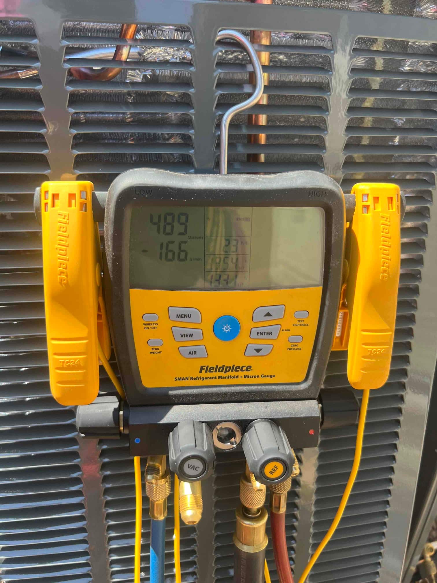 Digital manifold attached to the outdoor unit shows operating pressures with low side at 166 PSI and high side at 489 PSI.