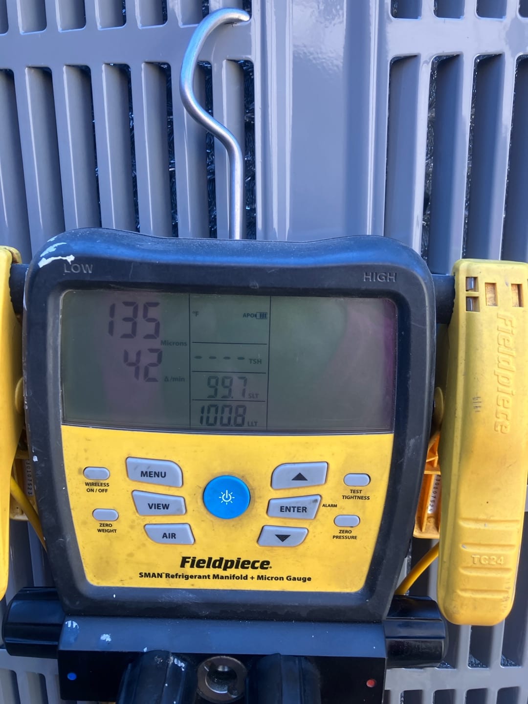 Digital manifold connected to the outdoor unit displays operating pressures with distinct low and high side readings during system commissioning.