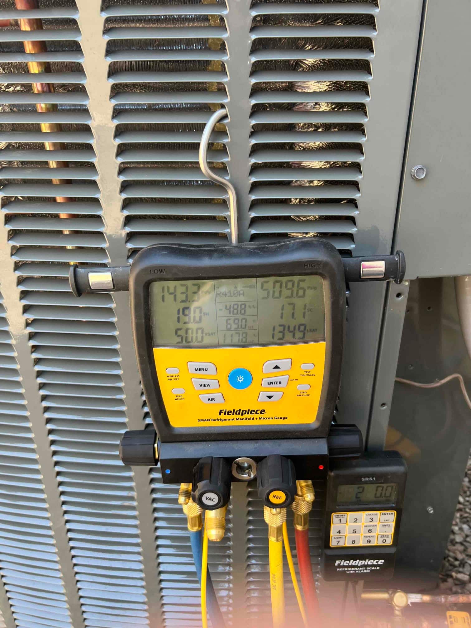 Digital manifold on an outdoor condenser shows operating pressures with hoses connected during system commissioning.