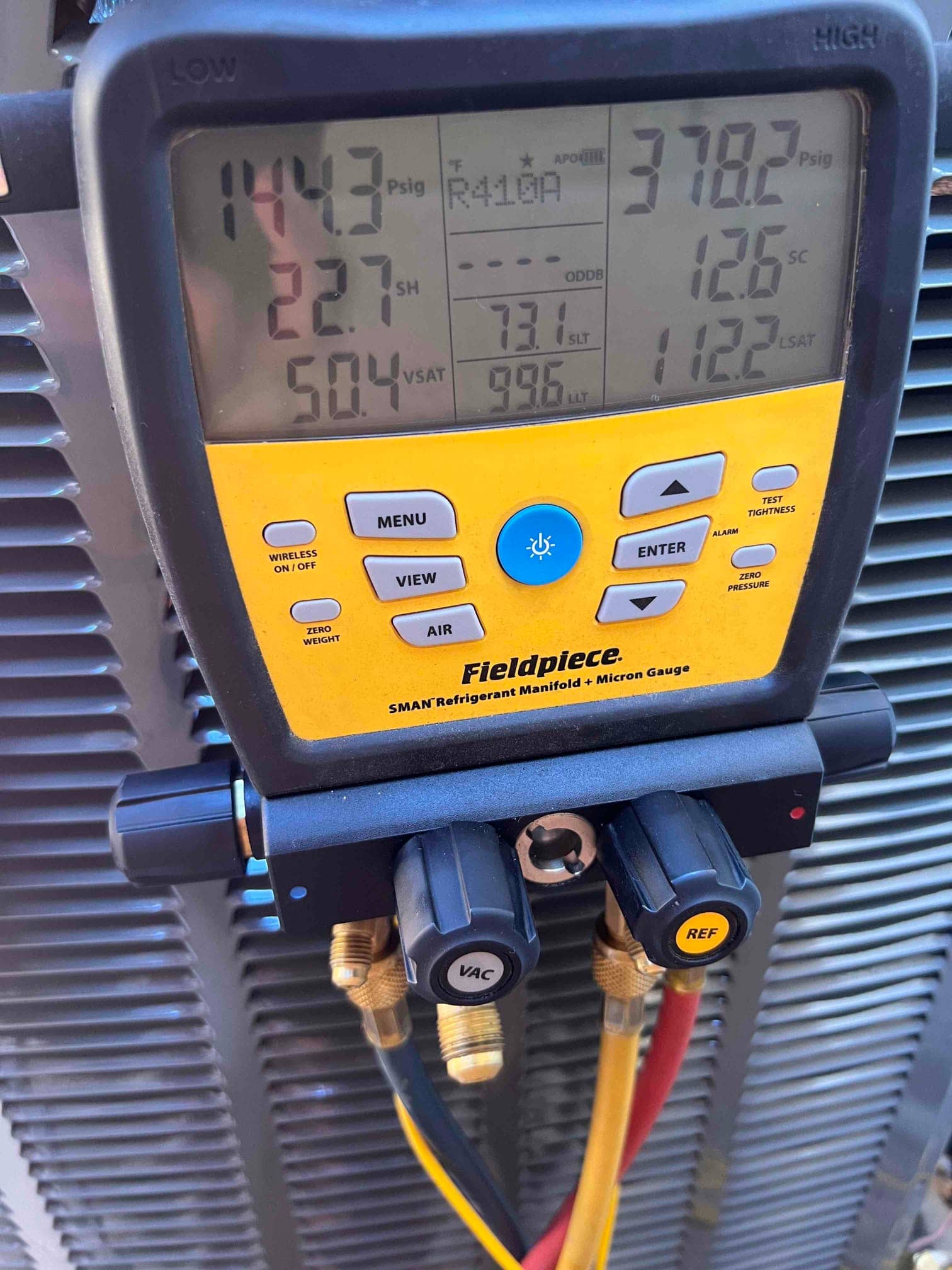 Digital manifold shows operating pressures while the condenser runs, with low and high sides connected during commissioning checks.