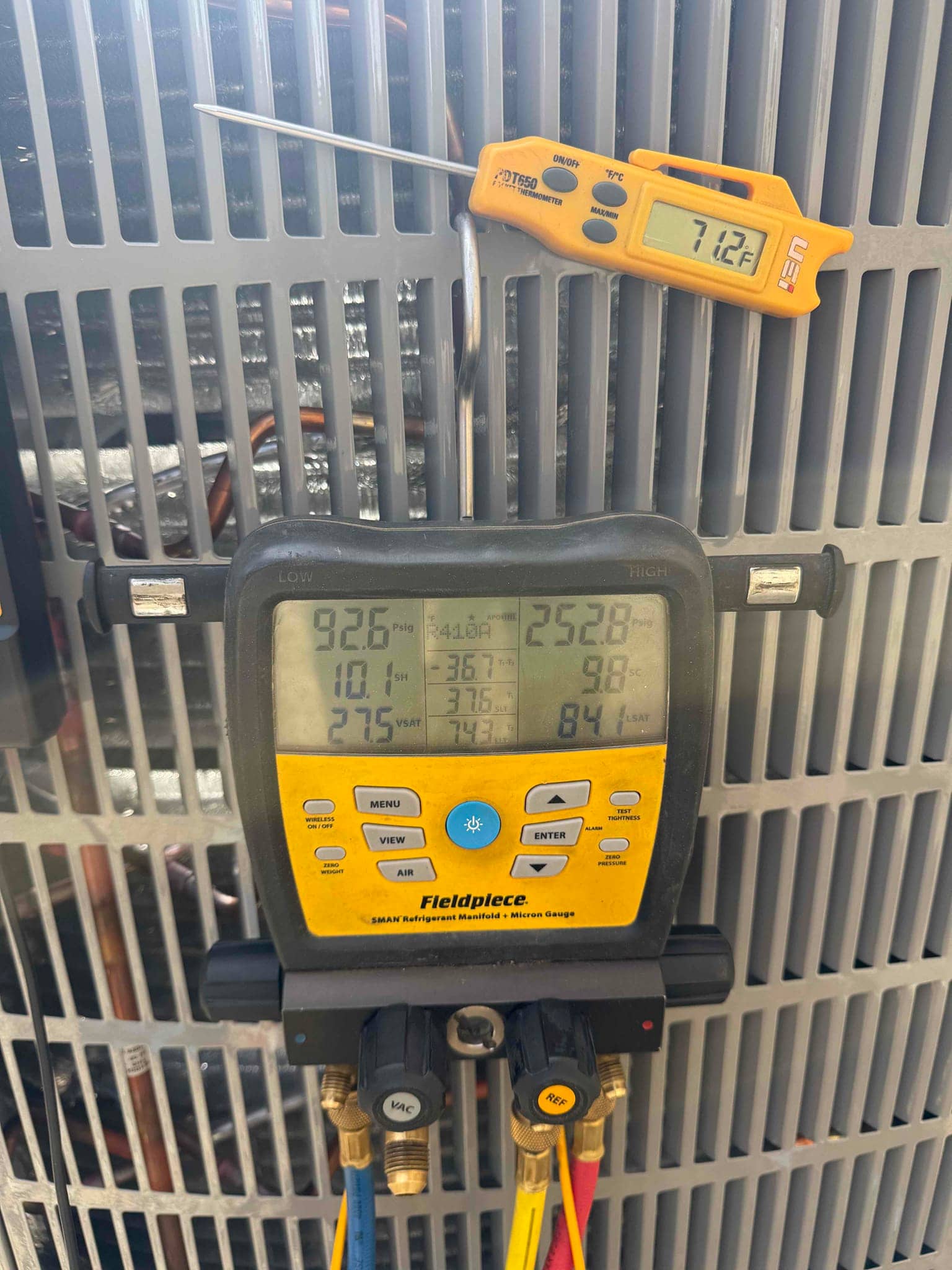Digital manifold shows operating pressures while a separate thermometer reads 71.2°F during system commissioning at the outdoor condenser.