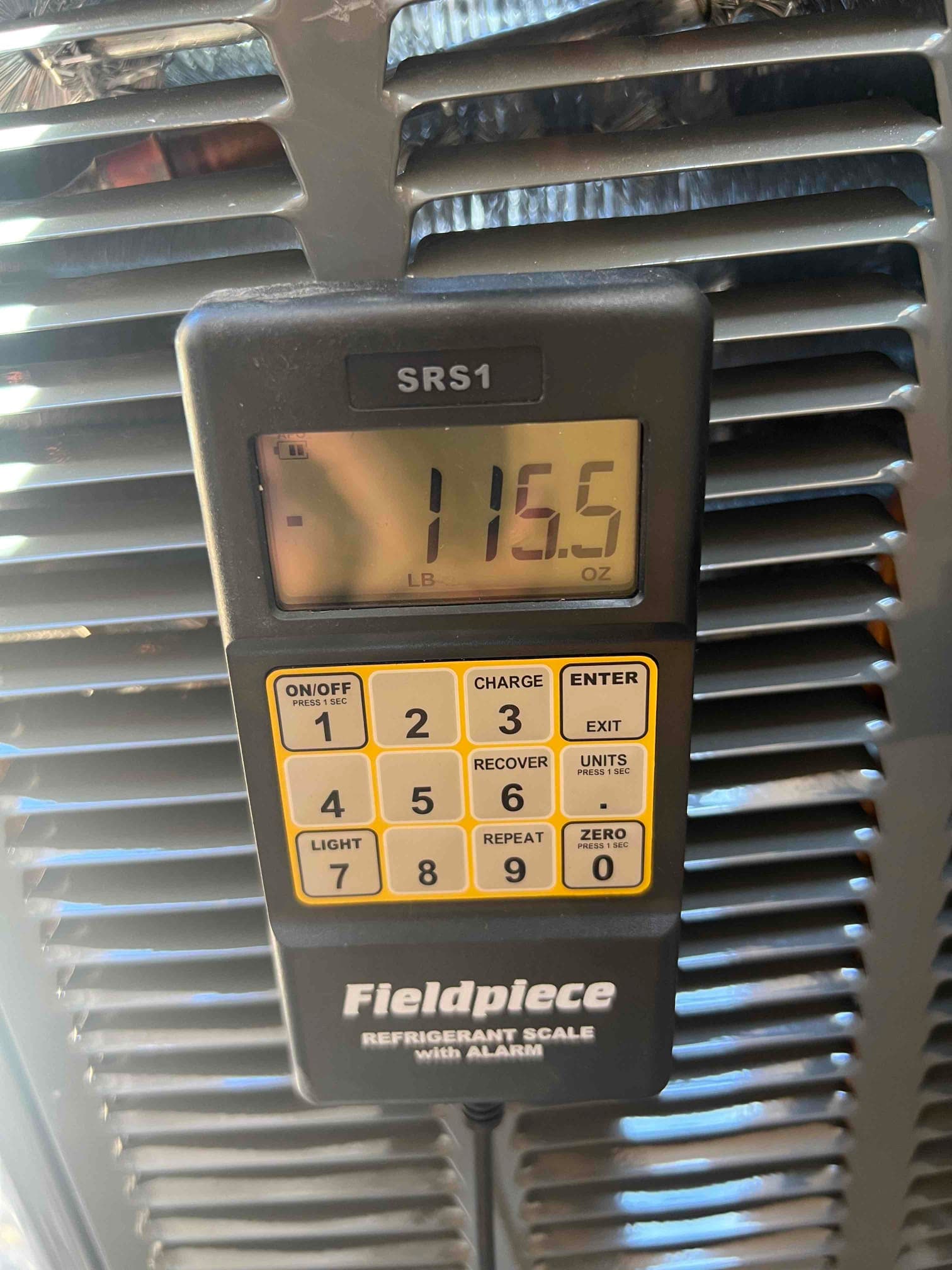 Digital refrigerant scale displays 115.5 ounces during charging at the outdoor condenser.