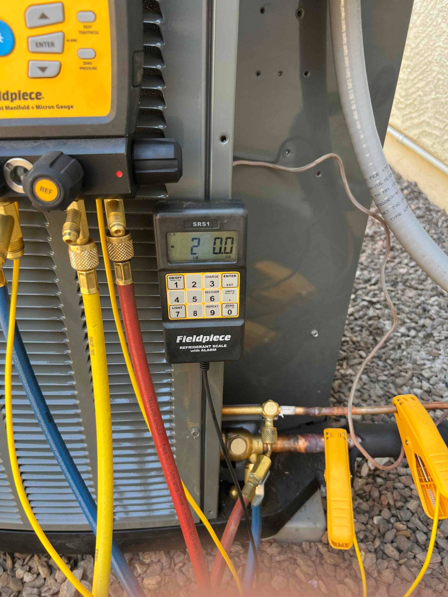 Digital refrigerant scale displays 2.0 pounds while manifold hoses connect to the outdoor unit during charging.