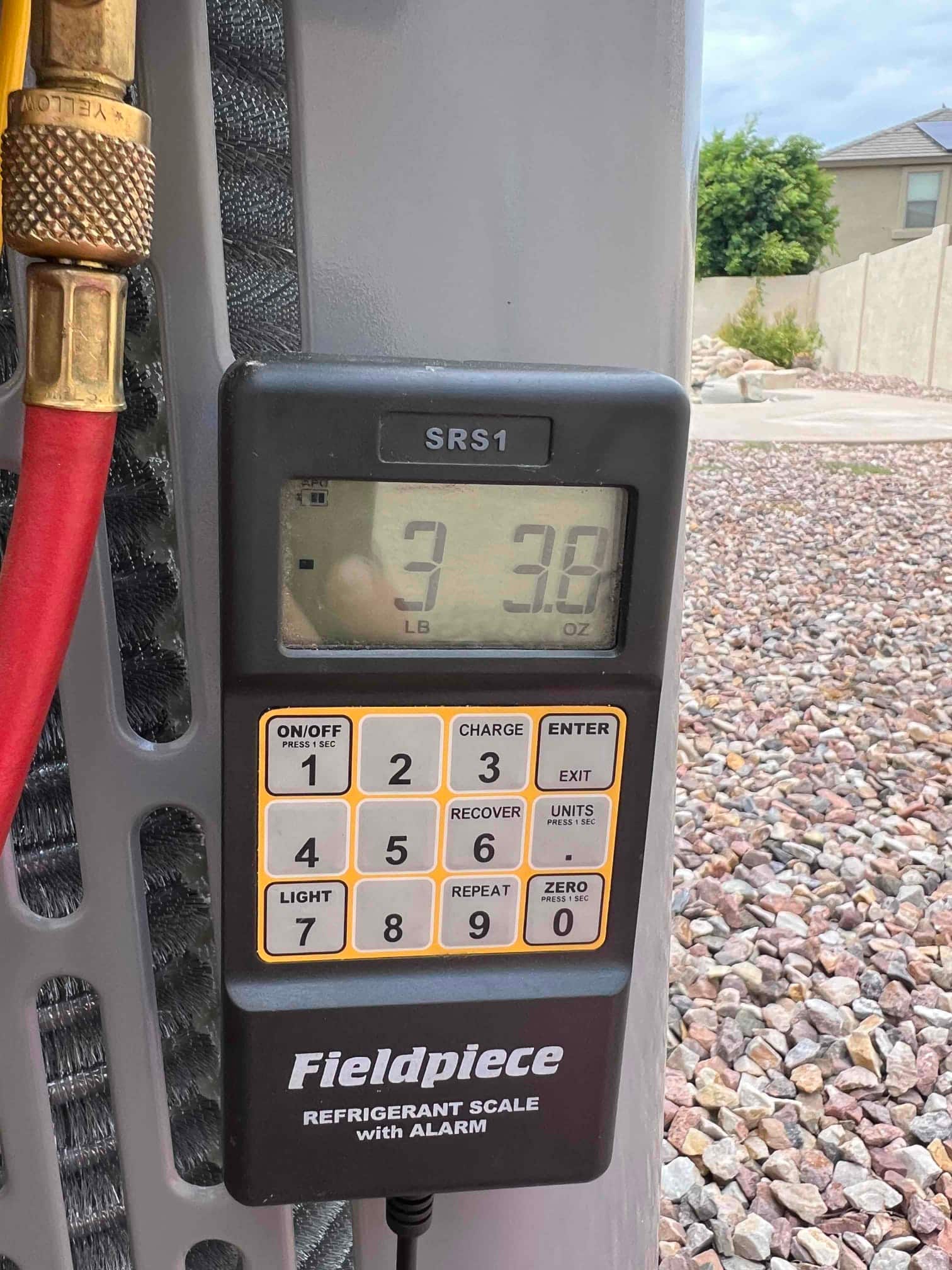 Digital refrigerant scale displays 3 pounds 3.8 ounces during charging beside the outdoor condenser coil and service hose.