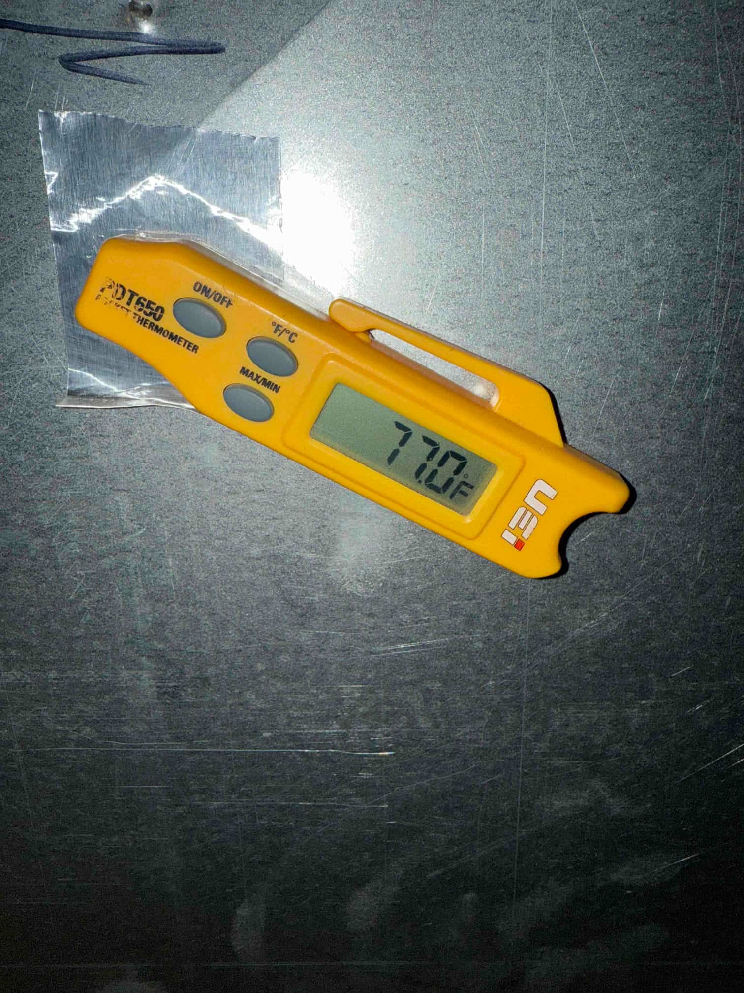 Digital thermometer displays 77.2 °F while measuring temperature on a metal HVAC surface during diagnostic work.