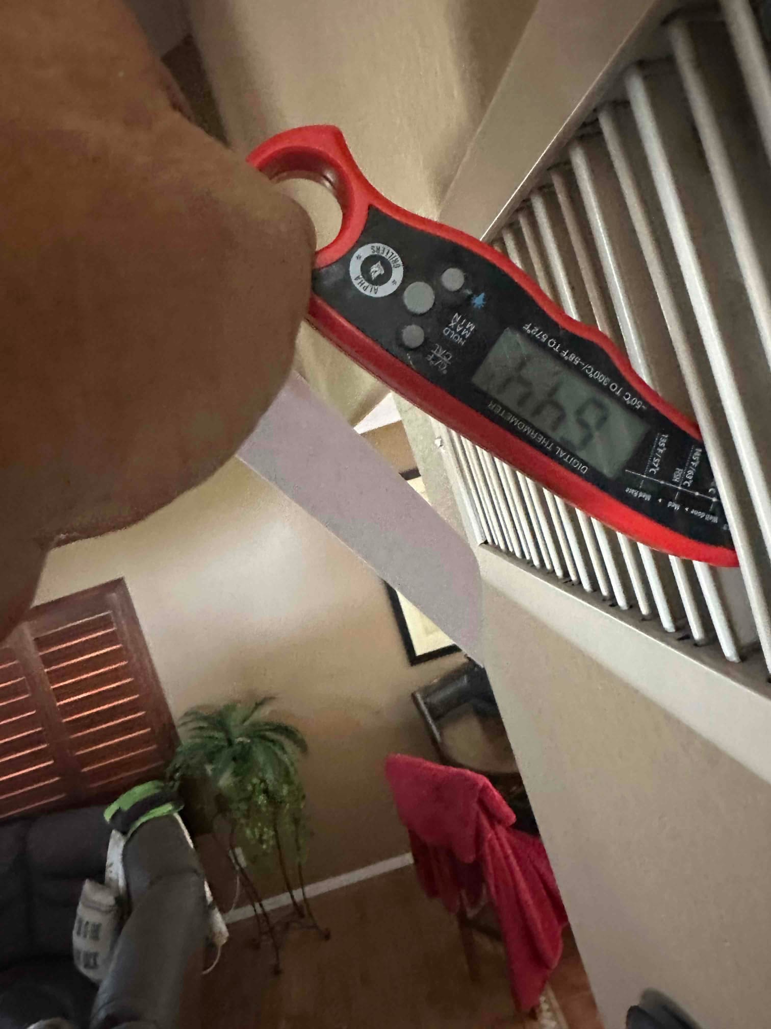 Digital thermometer inserted at a return grille shows indoor air temperature during HVAC commissioning.