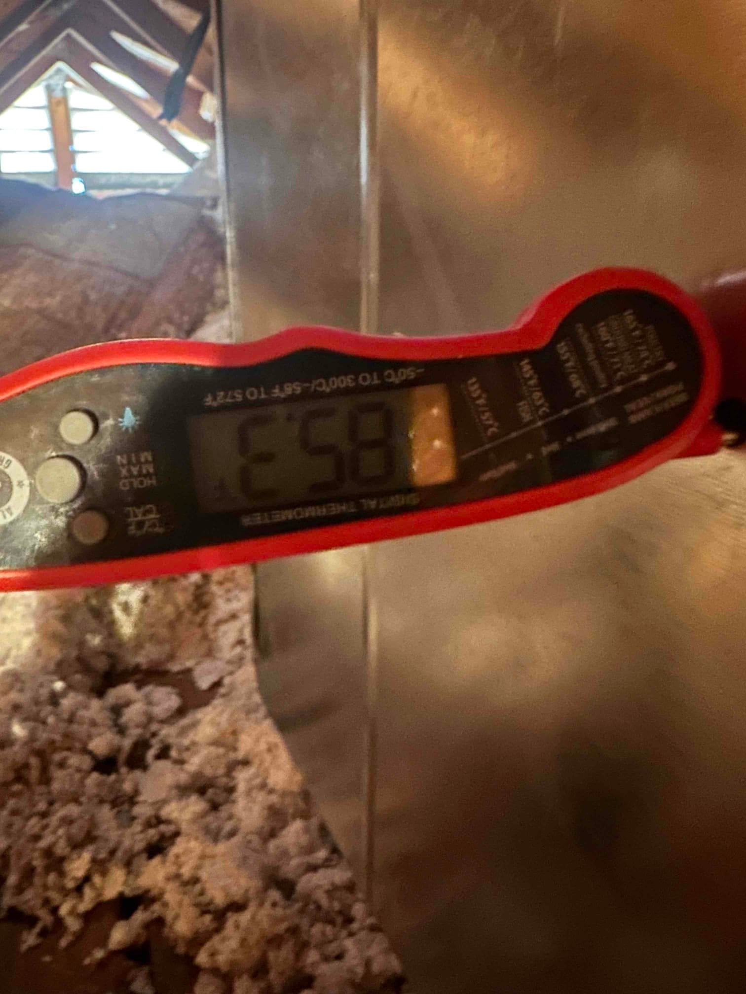 Digital thermometer at a metal duct in the attic shows 58°F, documenting supply air temperature after cooling.