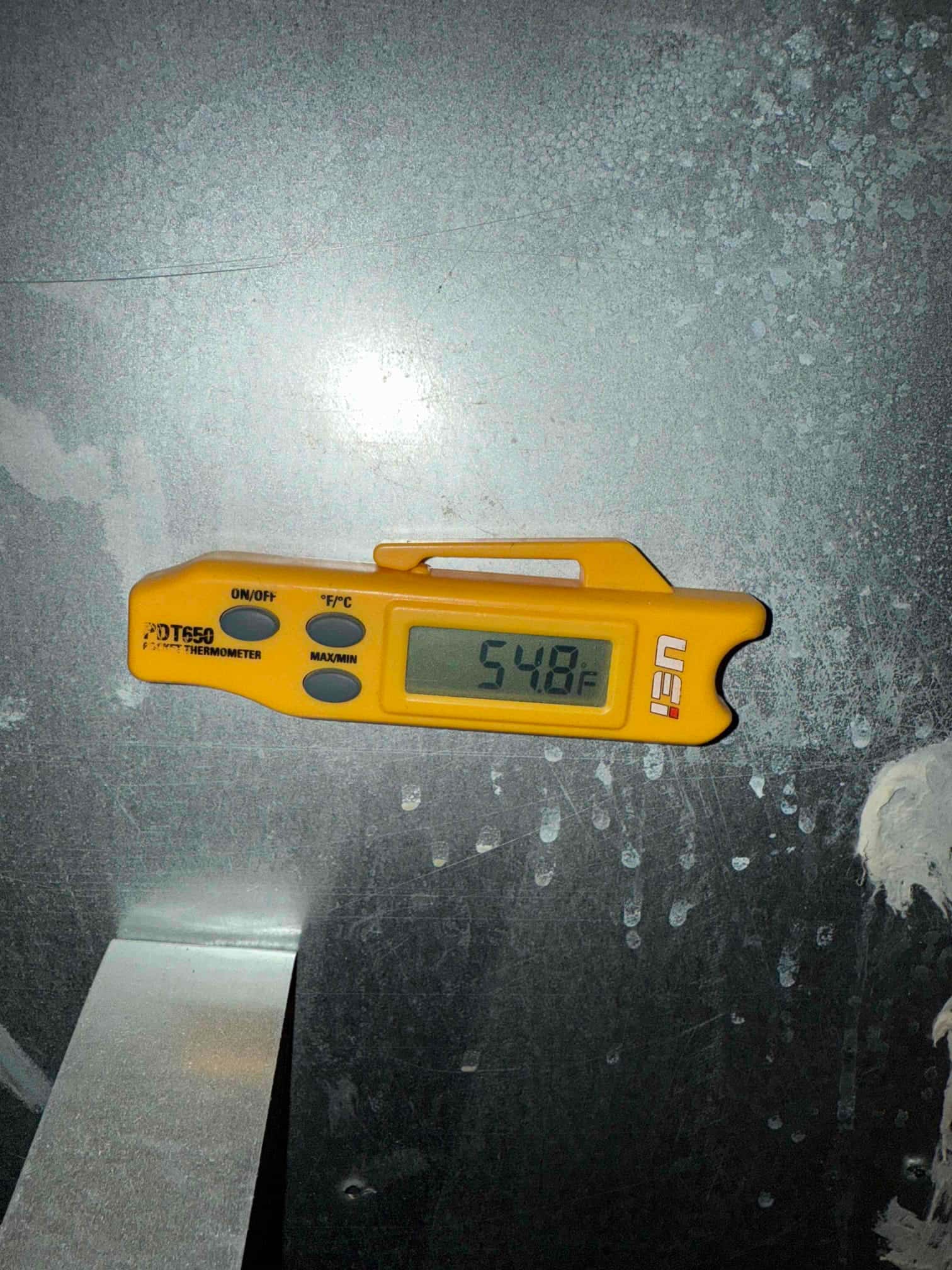 Digital thermometer on a metal HVAC surface shows 54.8 °F, indicating the measured surface temperature.