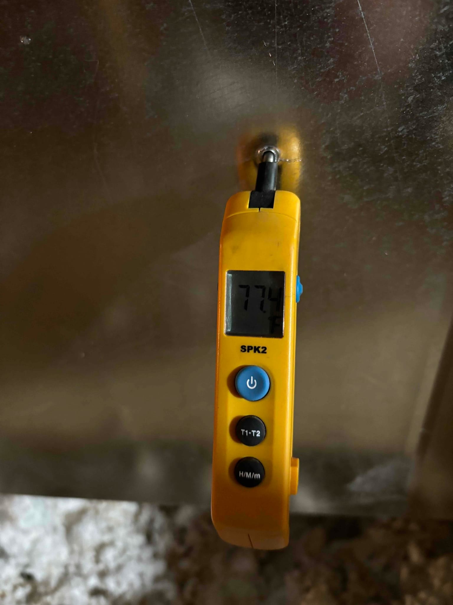 Digital thermometer probe inserted into duct reads 77.4°F, documenting return air temperature during air-side commissioning.
